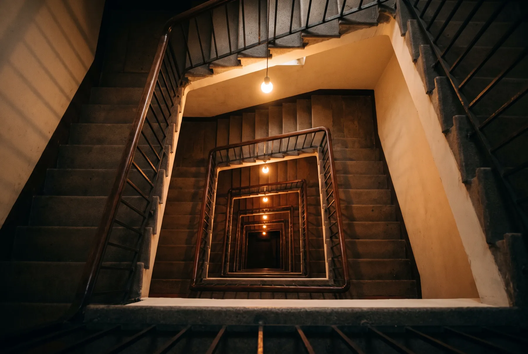 Blick von oben in einen alten Treppenschacht, die Läufe drehen sich in immer dunkleren Runden nach unten.